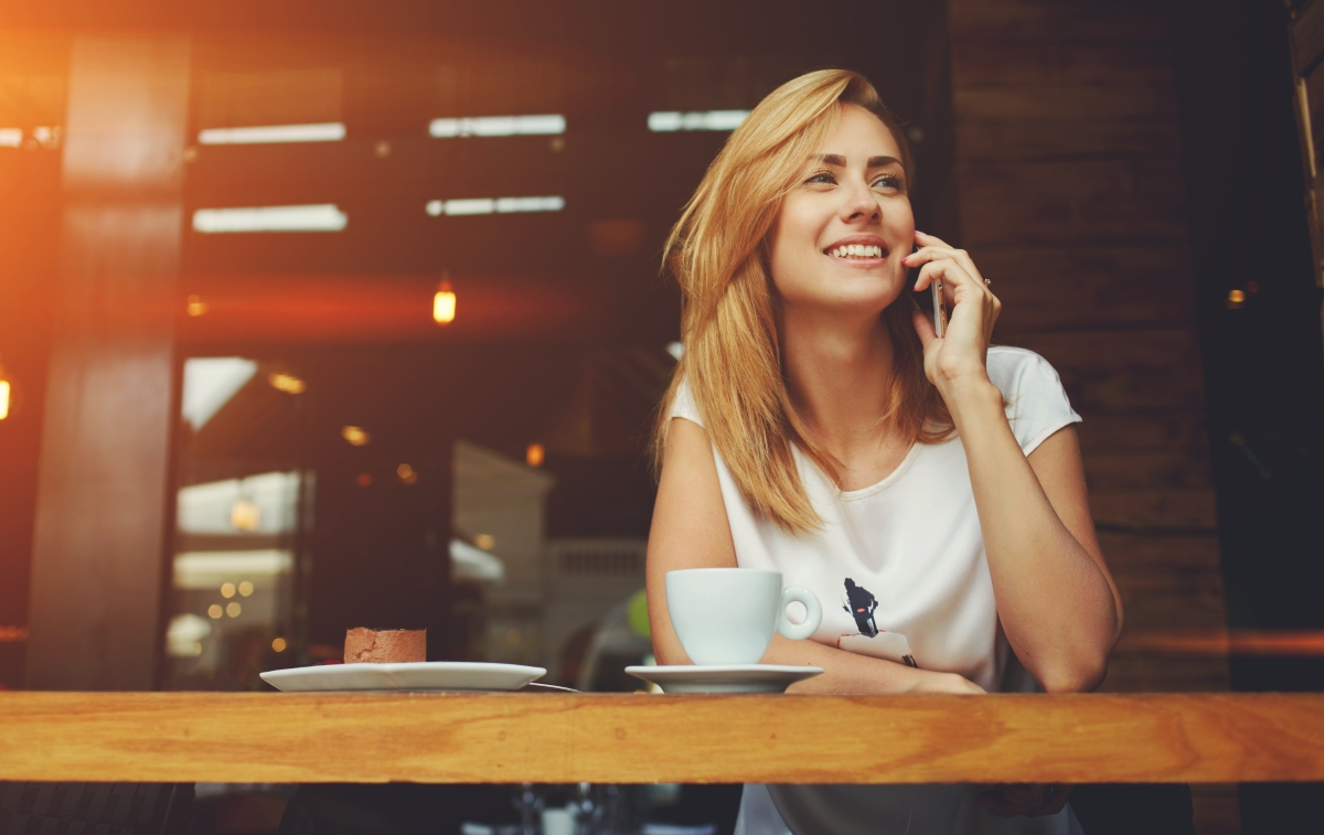Blonde Frau telefoniert in einem Caf&eacute; mit ihrem Handy