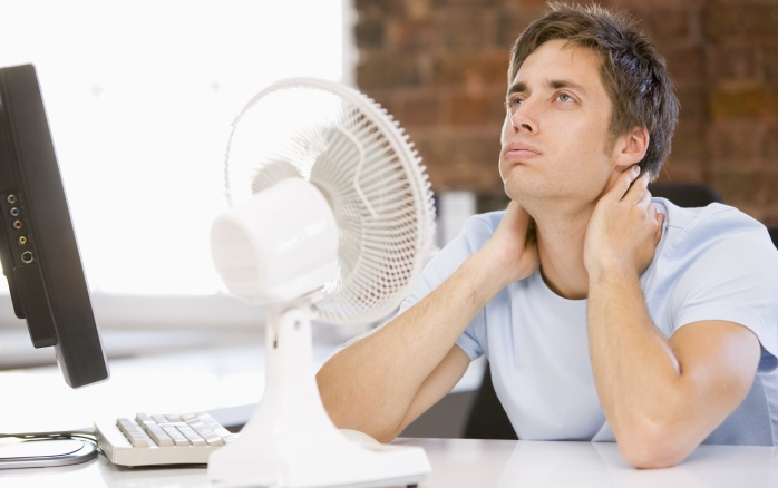 Mann im B&uuml;ro und verschafft sich mit Hilfe eines Ventilators K&uuml;hlung