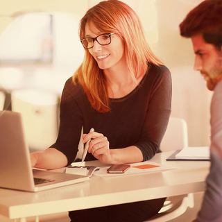 Frau und Mann sitzen am Bürotisch und blicken gemeinsam auf Computerbildschirm