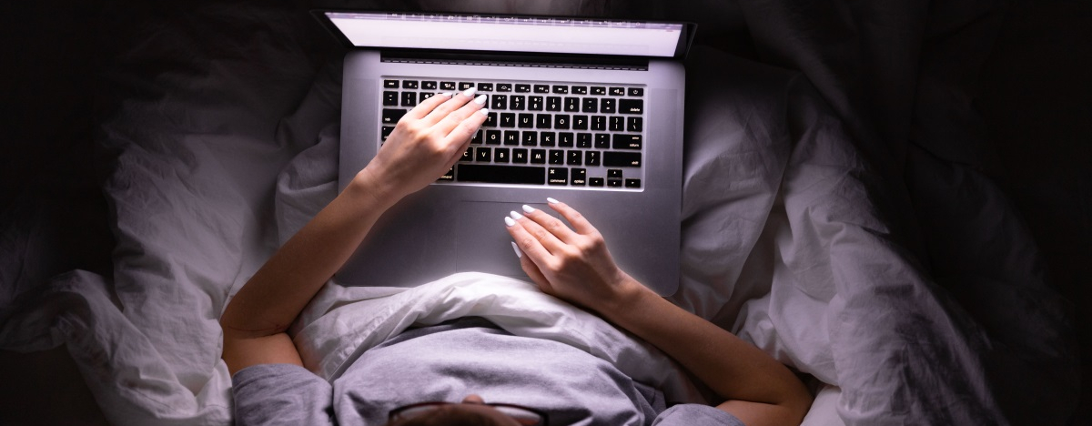 Frau sitzt in der Nacht mit Laptop im Bett