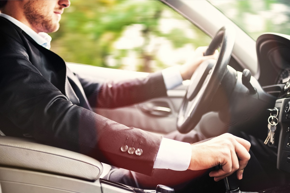 Seitliche Ansicht von einem Mann im Anzug, der im Auto sitzt und f&auml;hrt