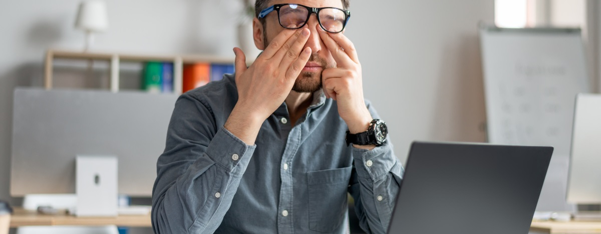 Mann im B&uuml;ro reibt sich die Augen vor M&uuml;digkeit
