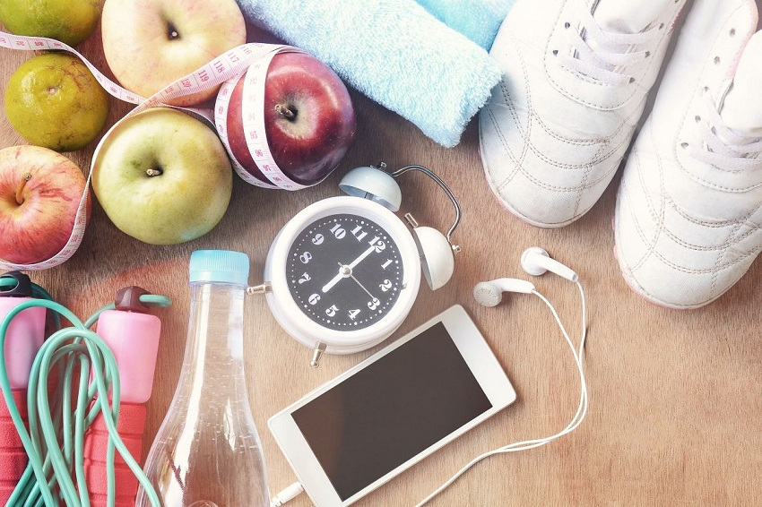 Zu sehen sind ein Handy, ein Wecker, ein paar wei&szlig;e Turnschuhe, ein Handtuch, &Auml;pfel, eine Flasche, ein Springseil und ein Ma&szlig;band.
