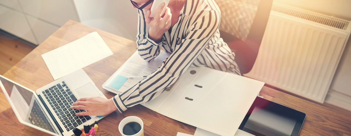 Business Frau sitzt daheim am Schreibtisch und telefoniert, w&auml;hrend sie an ihrem Laptop arbeitet