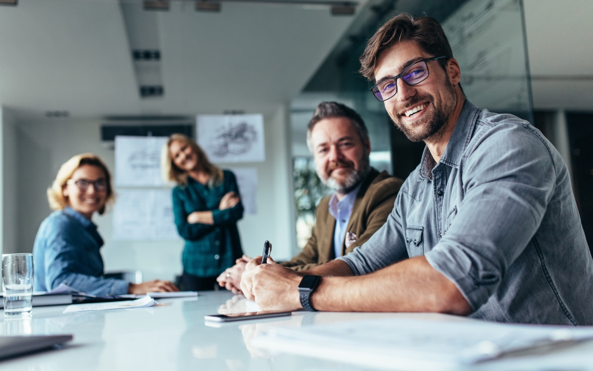Vier l&auml;chelnde Kollegen und Kolleginnen an einem Tisch, die sich beraten.