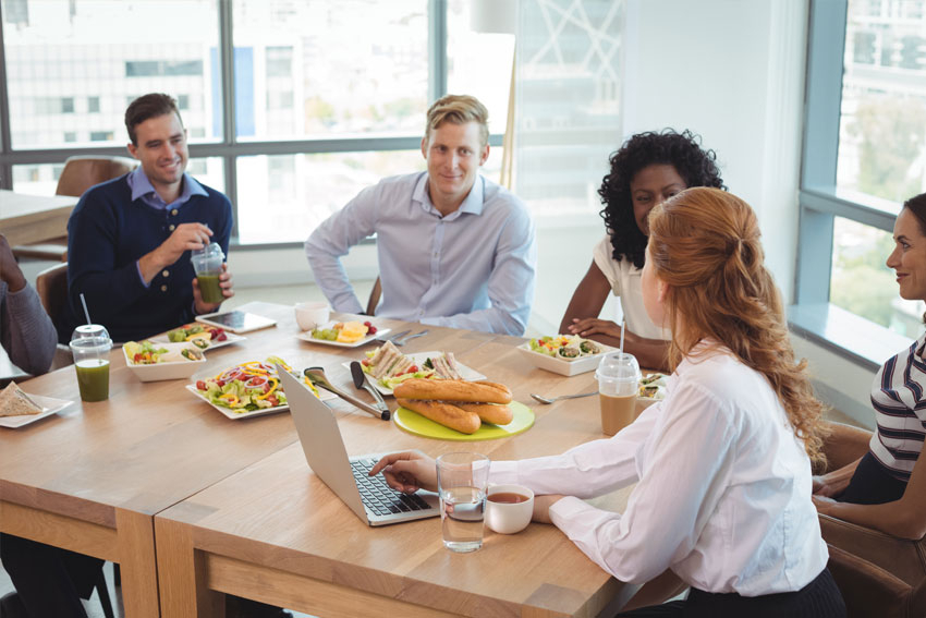 Arbeitskollegen diskutieren am Tisch, auf dem gesundes Essen steht
