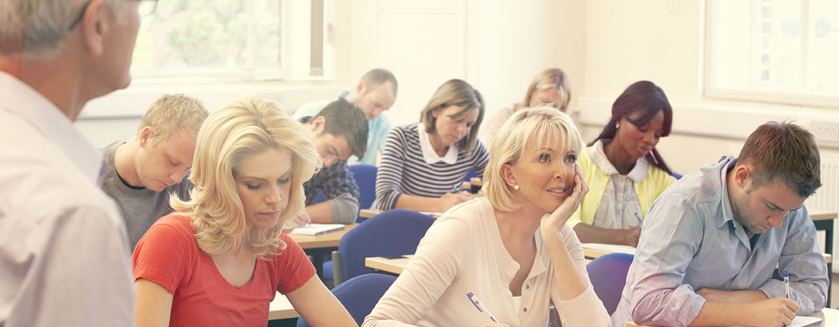 Frauen und M&auml;nner sitzen in einem Klassenraum und schreiben etwas von einer Tafel ab