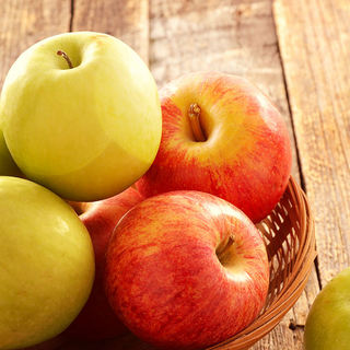 Kleiner Korb mit gr&uuml;nen und roten &Auml;pfeln auf einem Holztisch