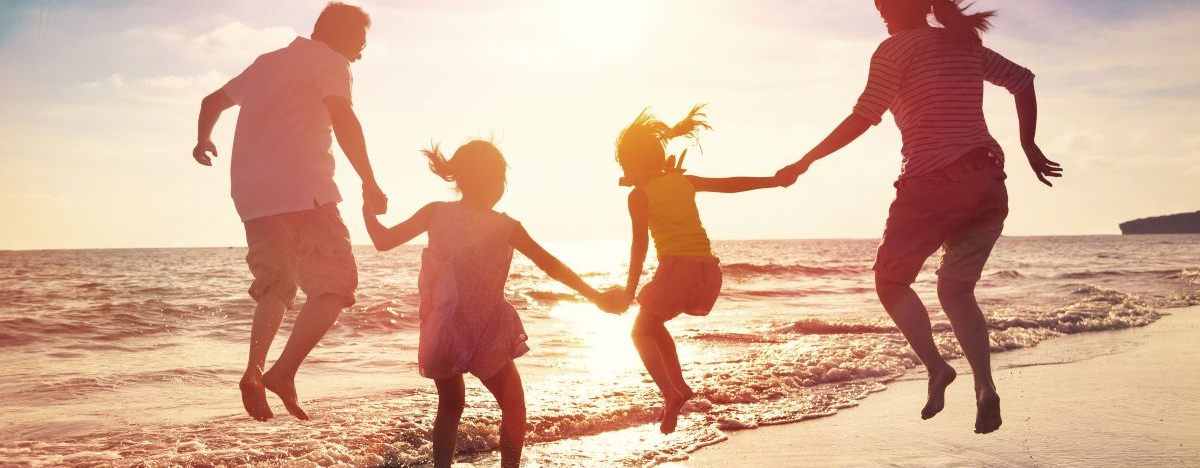 Vierk&ouml;pfige Familie h&uuml;pft am Strand bei Sonnenuntergang