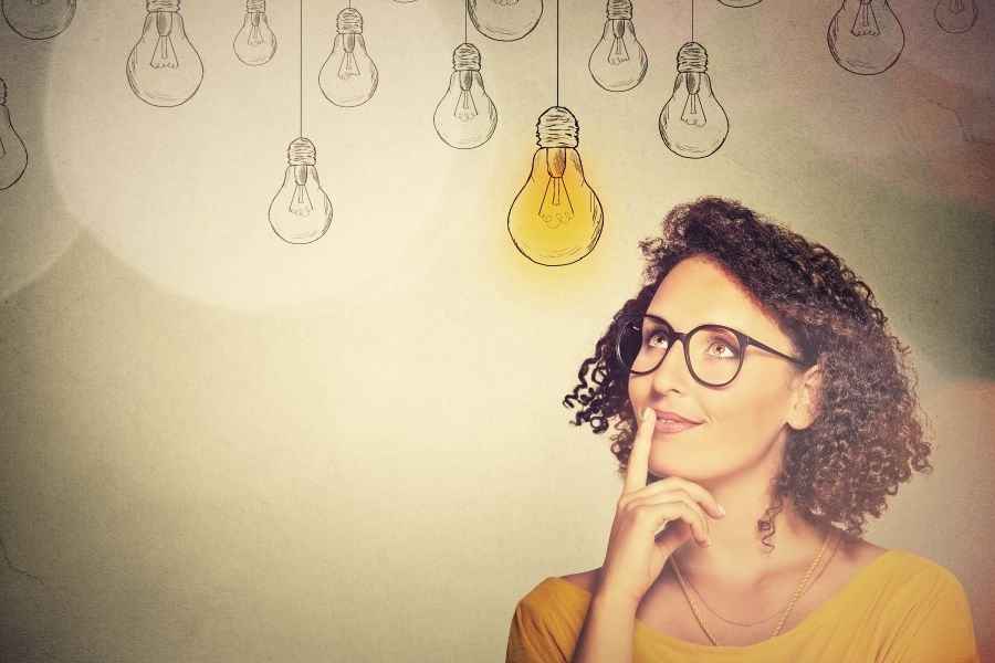 Ein Bild einer Frau die nachdenklich in die Ferne schaut, &uuml;ber ihr eine leuchtende Gl&uuml;hlampe.