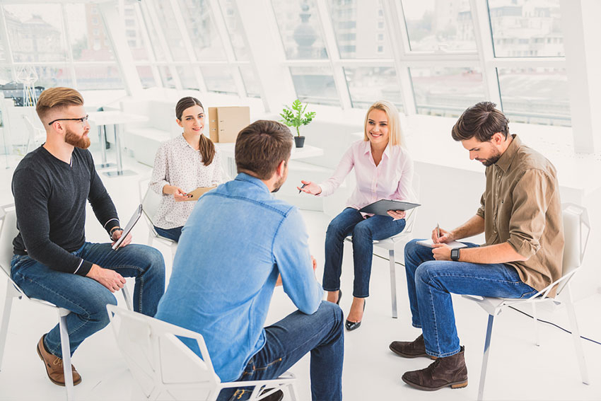 F&uuml;nf Personen sitzen auf St&uuml;hlen in einem Kreis