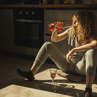Rothaarige Frau sitzt auf dem K&uuml;chenboden und trinkt Wein aus der Flasche