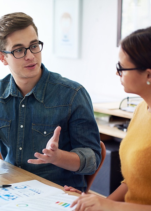 Ein junger Mann und eine junge Frau sitzen an einem Tisch und sprechen miteinander