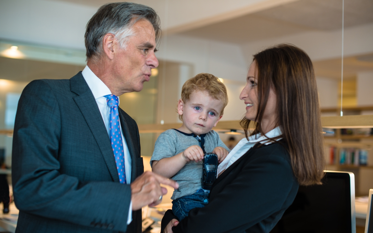 Chef mit Mitarbeiterin, die ein kleines Kind auf dem Arm tr&auml;gt