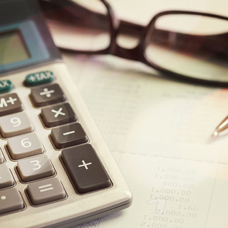 Nahaufnahme mit Taschenrechner, Brille und Kugelschreiber