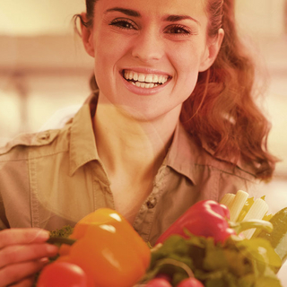 Junge Frau h&auml;lt einen Korb mit Gem&uuml;se und lacht in die Kamera